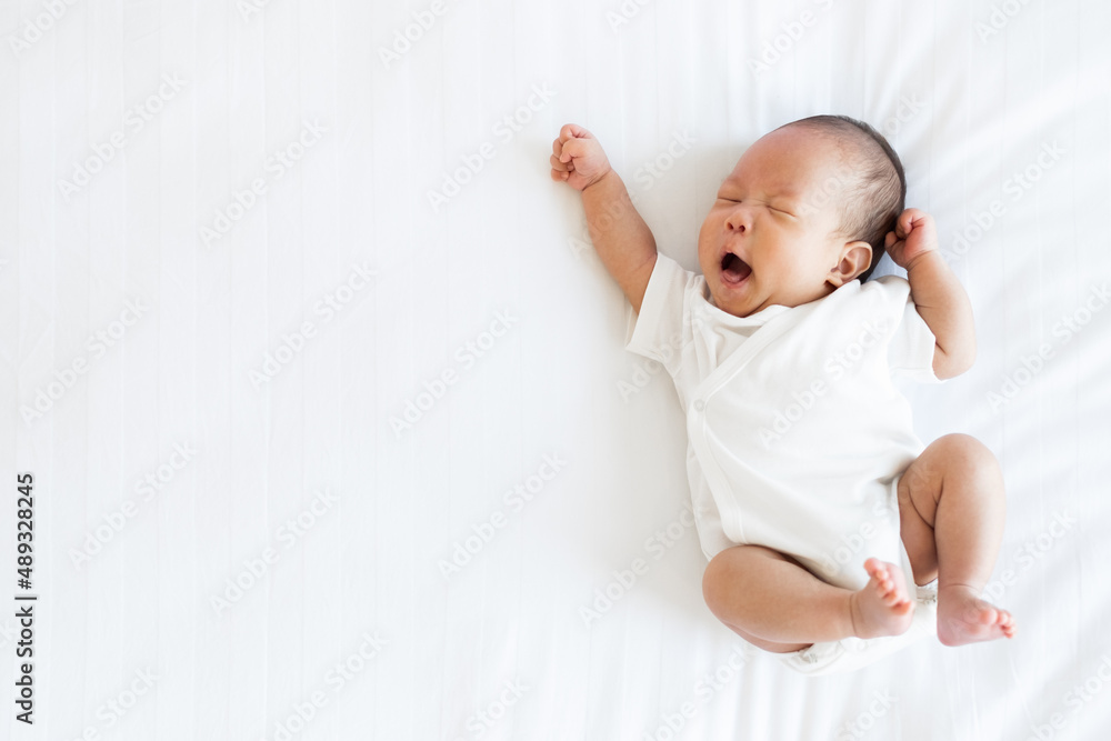 Portrait of Asian newborn baby in white cloth on bed funny pos