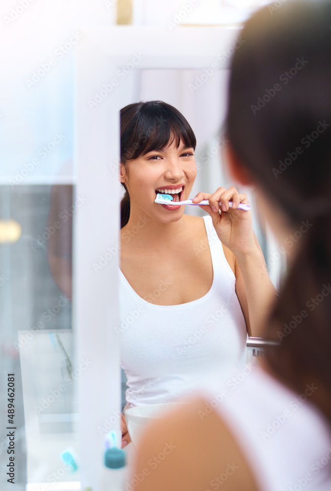 保持珍珠洁白。一个快乐迷人的年轻女子一边刷牙一边看的照片