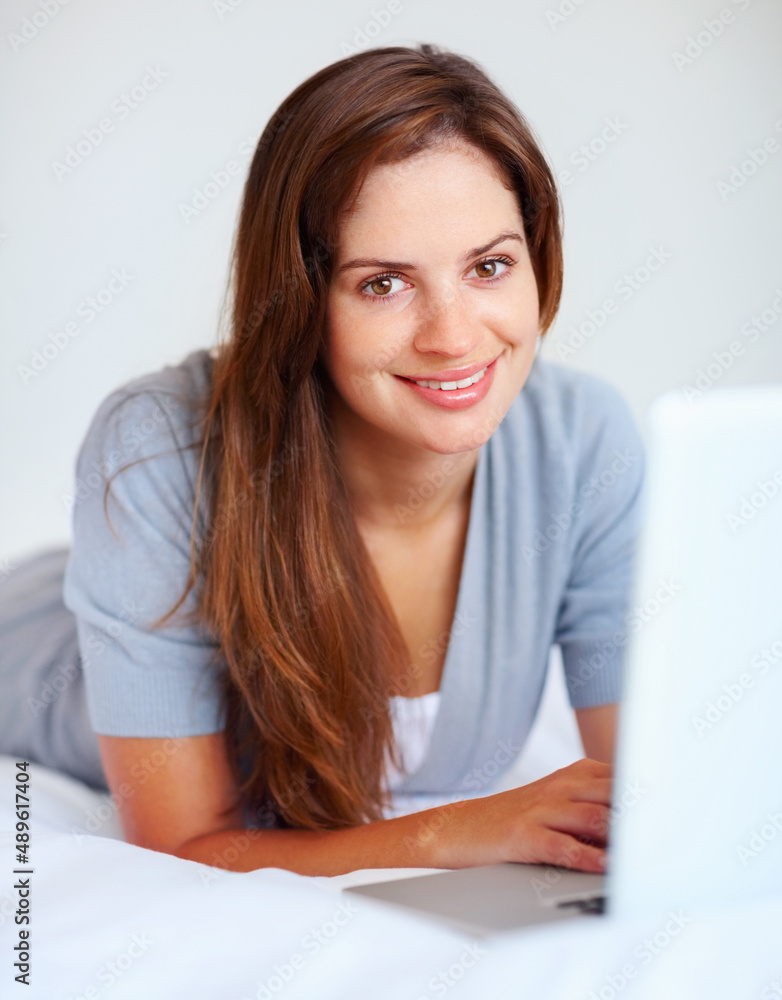 快乐的漂亮女人在床上用笔记本电脑。一个可爱的年轻女人在睡觉时用笔记本电脑的画像