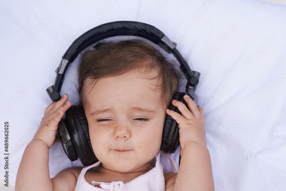听摇篮曲。一个可爱的小女婴戴着耳机听音乐。