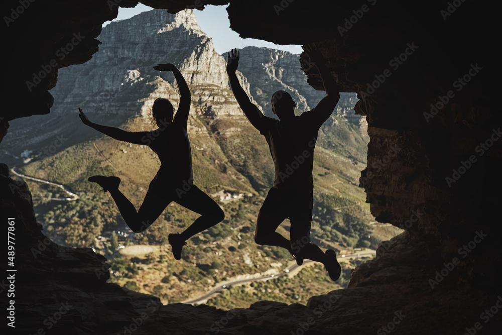 我们做到了。一对年轻夫妇在山上徒步旅行时兴奋地跳起来的后视镜头。
