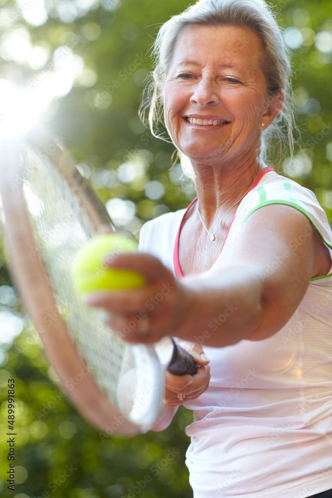 我有多年的练习来完善我的发球。微笑的资深女子正准备发球——网球。