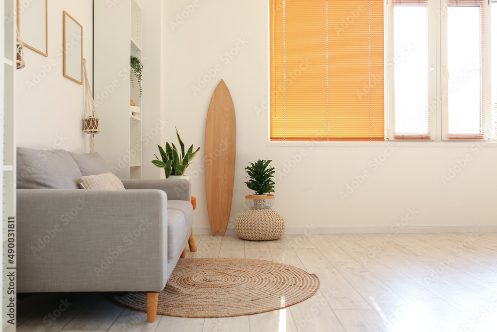 带木质冲浪板、室内植物和沙发的浅色客厅内部