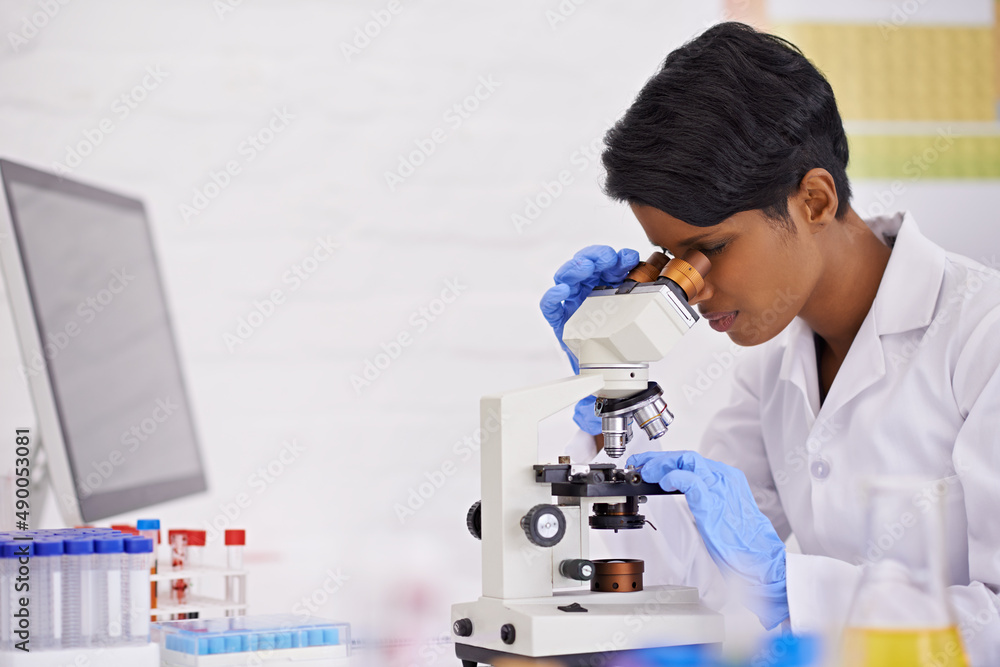 工作中的完美主义者。一位年轻的科学家在实验室的办公桌上使用显微镜。