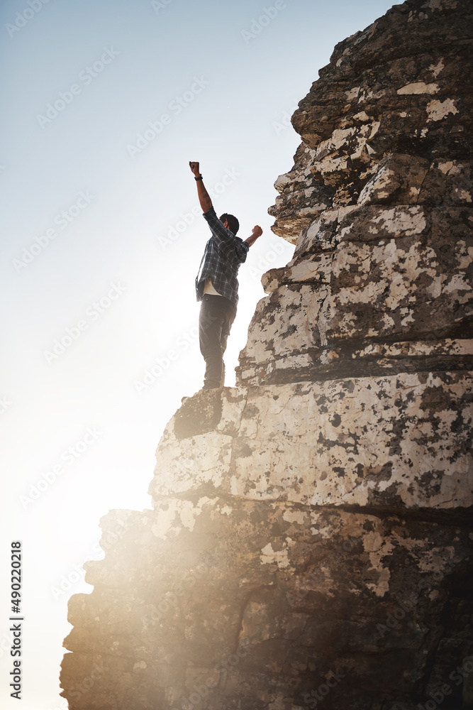 我是世界之王。照片中一个年轻人举起双臂站在悬崖上。