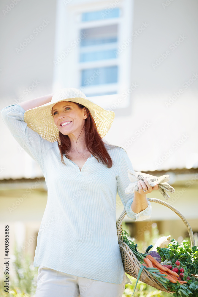 园艺是我放松的方式。一位漂亮的女士拿着她的园艺手套和一篮新鲜采摘的蔬菜