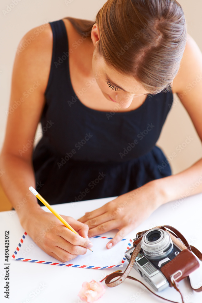 写回家。一个年轻女人在信封上写地址，桌子上放着一台相机。