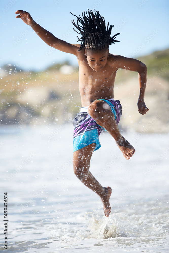 飞溅。一个兴奋的小男孩在海滩上跳到空中。