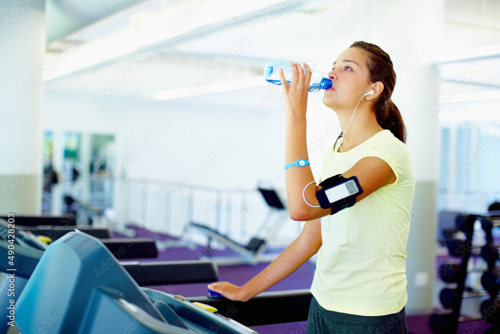 Young woman drinking water. Young woman standing on treadmill and drinking water.