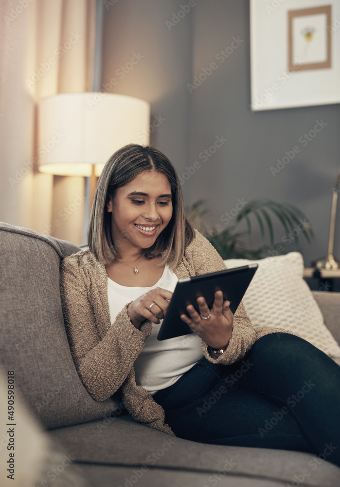 把她的平板电脑变成迷你电视。一个年轻女人在家里的沙发上使用数字平板电脑的镜头。