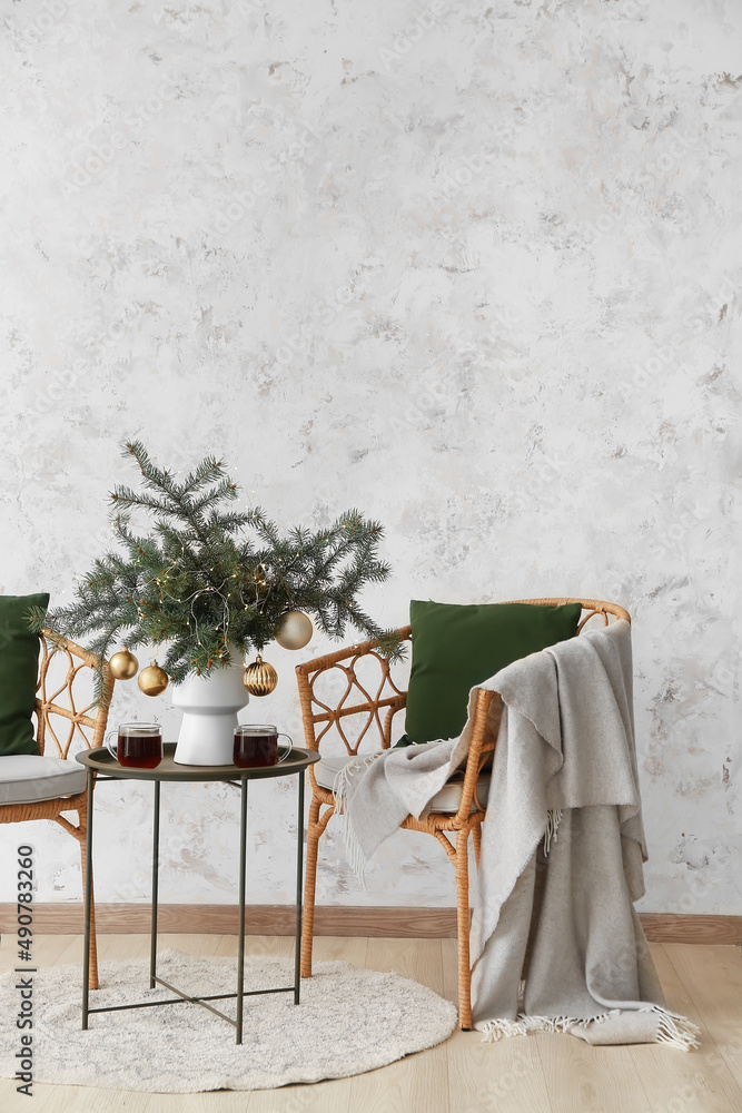 花瓶里有圣诞球的冷杉树枝，浅色墙壁附近的桌子和椅子上有几杯茶