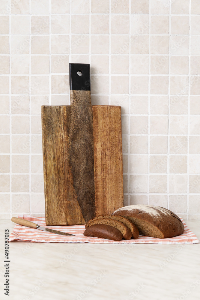瓷砖墙附近桌子上的木制砧板和面包