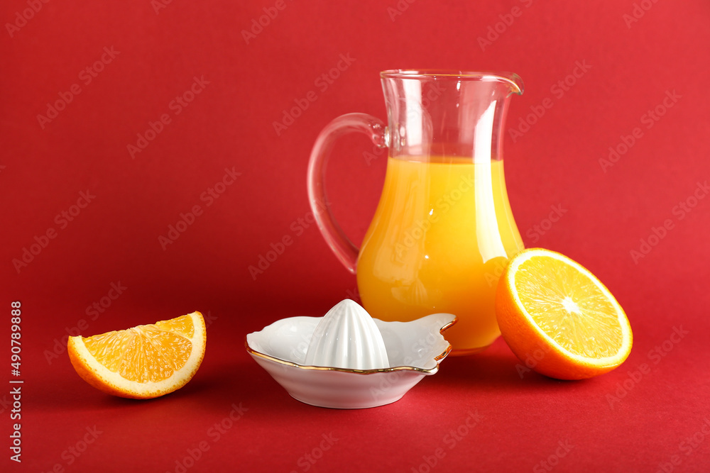 陶瓷榨汁机，红色背景上的一罐果汁和橙子