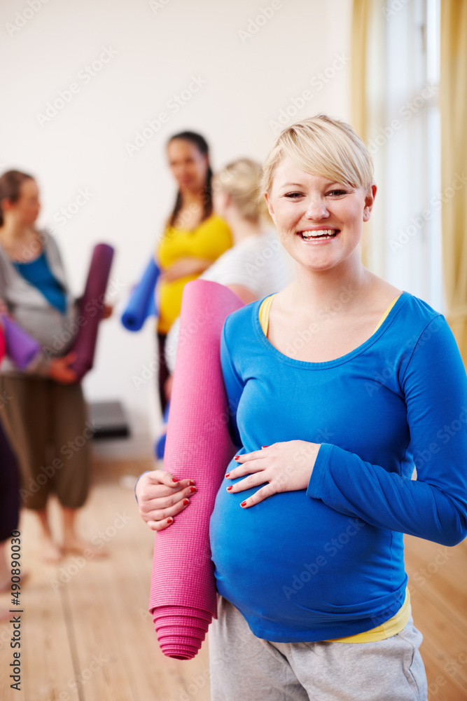 为我的孩子保持健康。一个年轻的金发孕妇在健身房里拿着运动垫。
