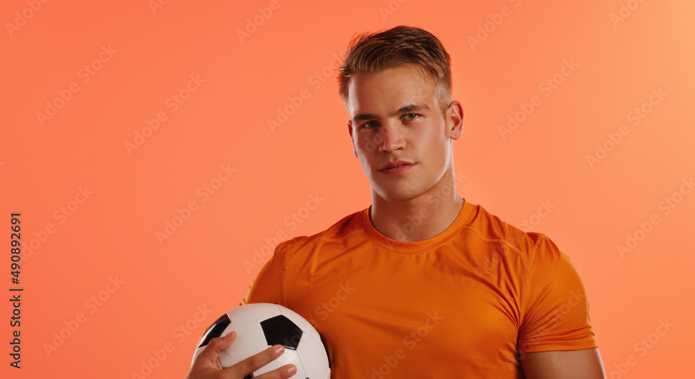 你掌握了技巧。一位英俊的年轻男子足球运动员拿着球摆姿势的工作室肖像。