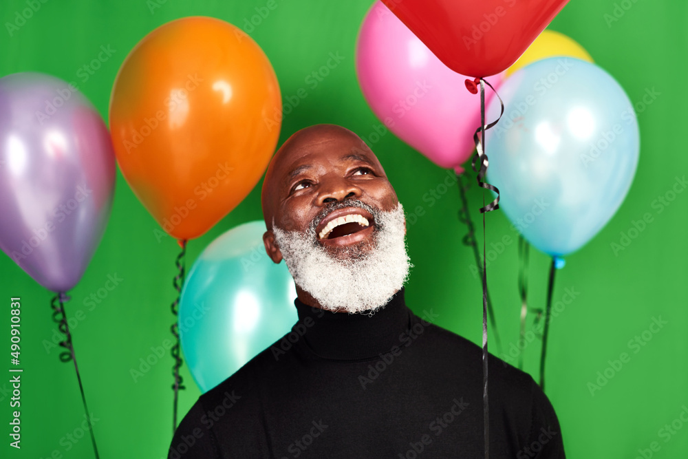 Live your life and be merry. Studio shot of a man posing against a green background with balloons ar
