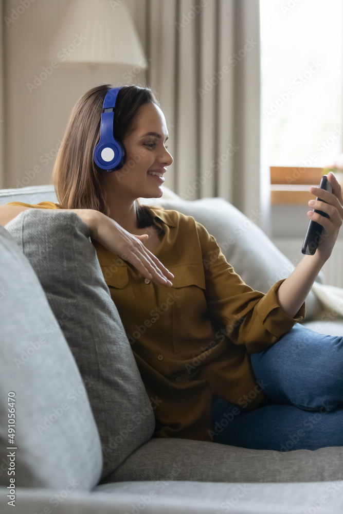 垂直图像微笑的年轻女性戴着耳机，手持智能手机观看最爱ar的视频片段