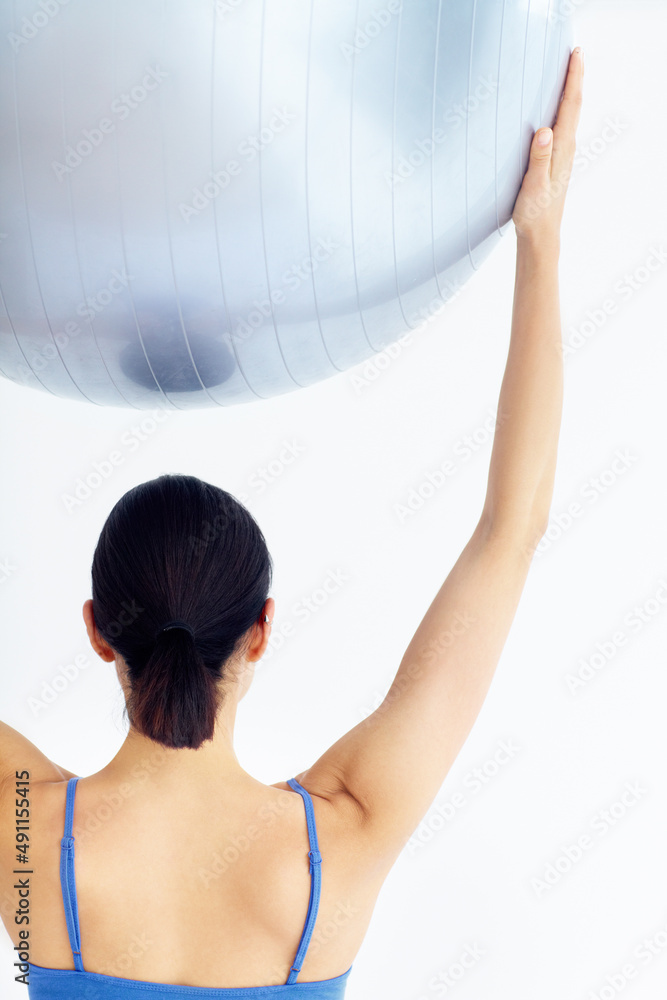 努力实现健康。一名年轻女子举起瑞士球的后视图。