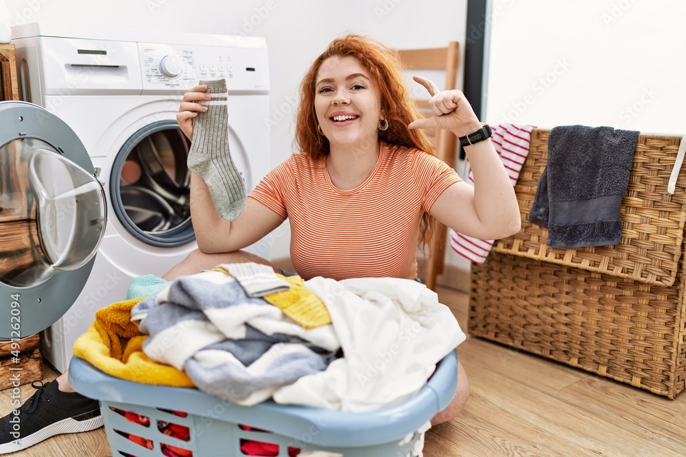 年轻的红头发女人把脏衣服放进洗衣机，面带微笑，自信地用手势