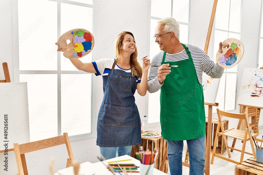 两位中年艺术家在艺术工作室拿着画笔和调色板开心地微笑着。