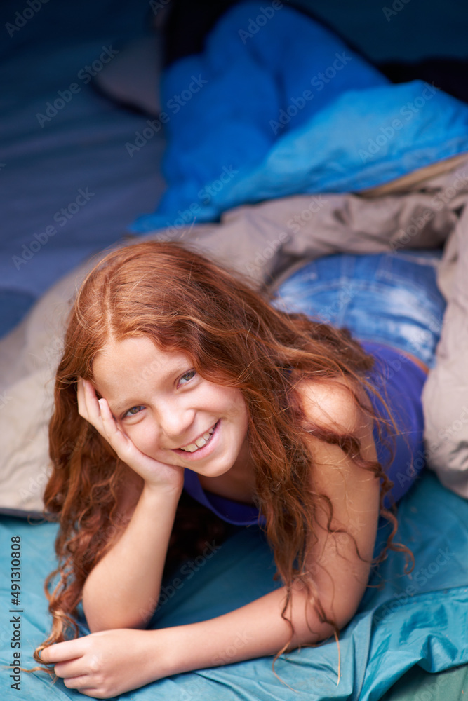 她喜欢露营。一个快乐的年轻女孩躺在帐篷里露营的画像。