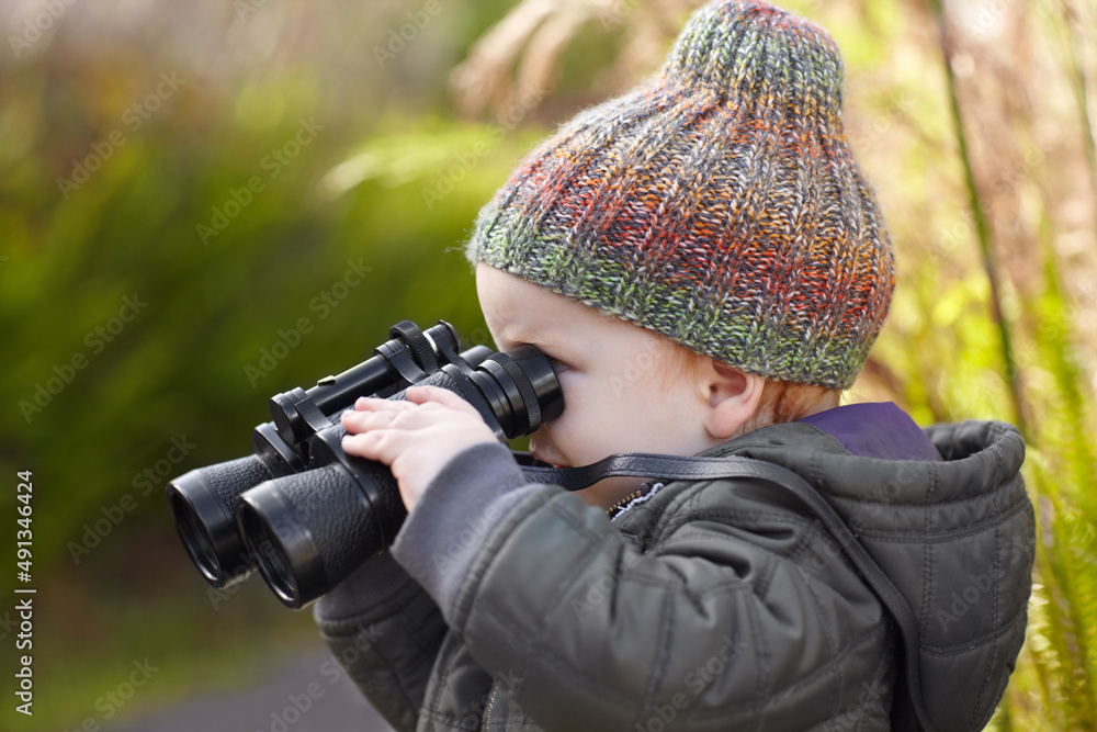 他越来越喜欢户外活动。一个可爱的小男孩用双筒望远镜看。