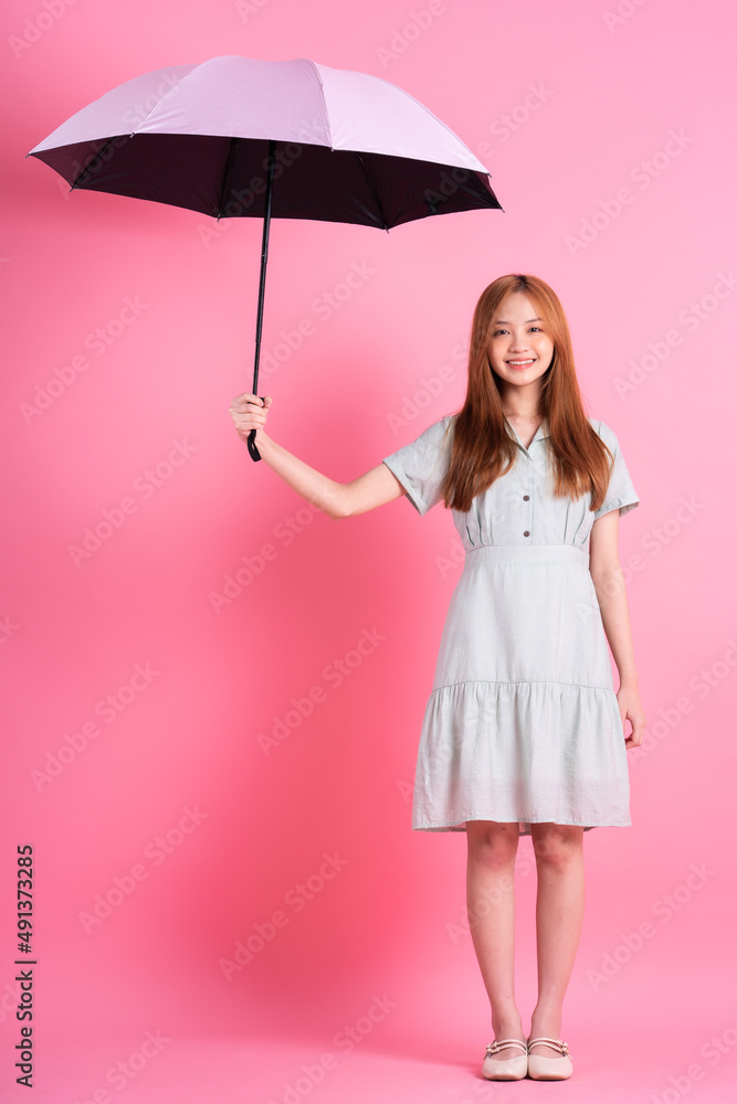 粉色背景下撑着雨伞的亚洲年轻女子