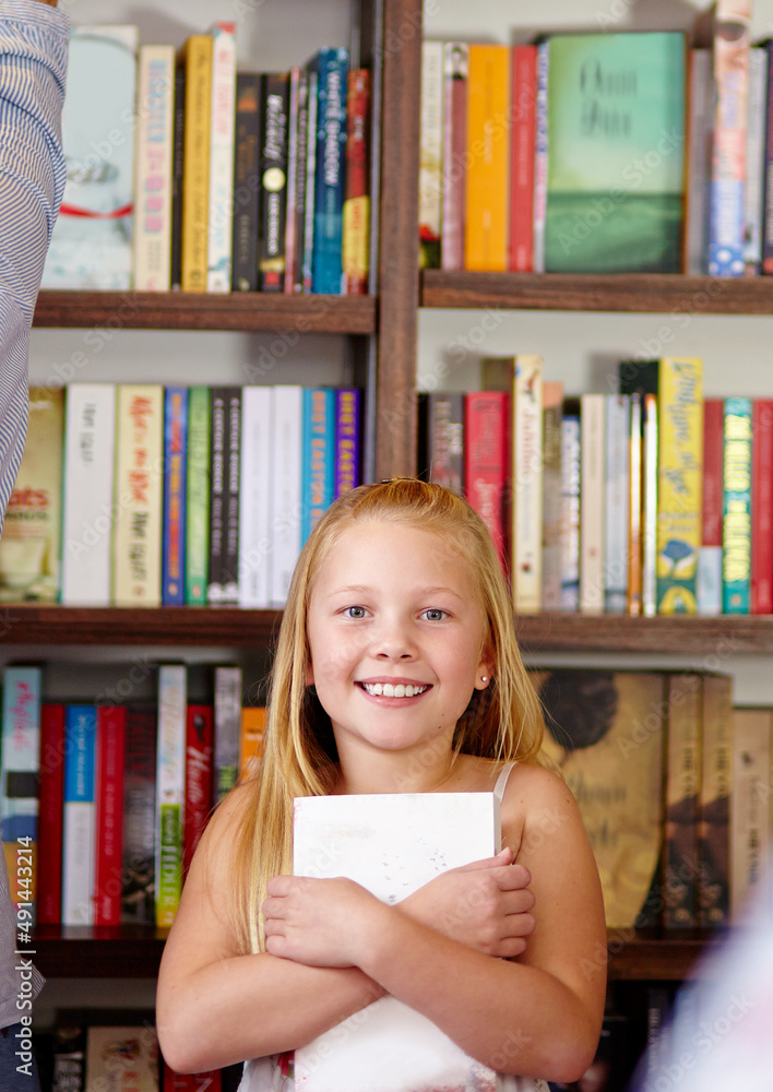 我喜欢书。一个可爱的年轻女孩在图书馆里抓着她的书。