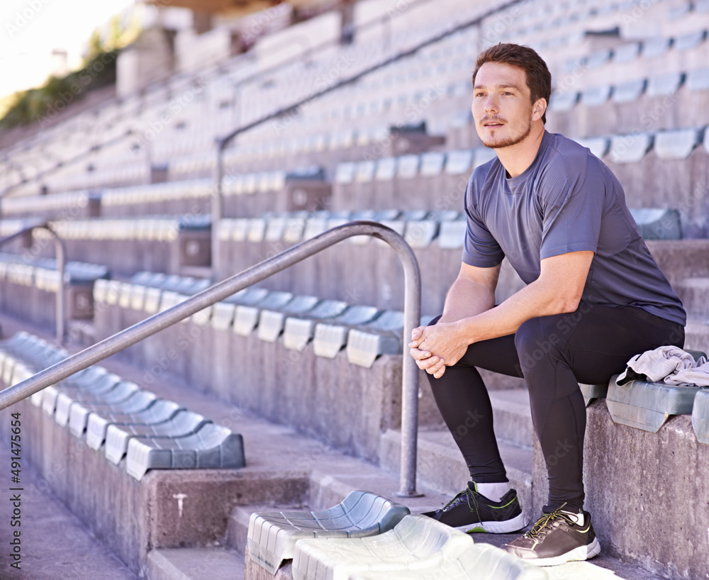 Taking it all in. Shot of a handsome young man sitting in the stands at an athletics arena.
