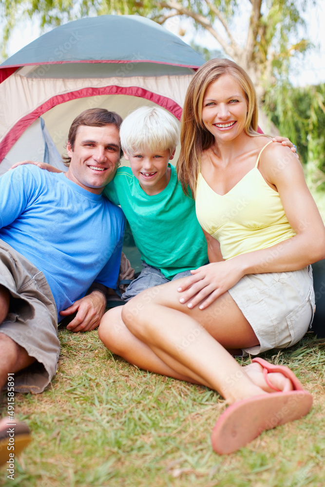 可爱的家庭露营。可爱的三口之家在帐篷前露营，面带微笑的肖像。