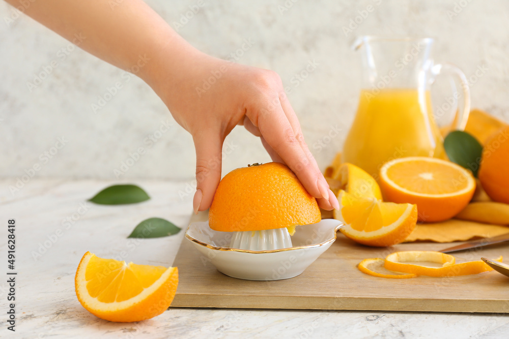 Woman squeezing fresh orange on light background