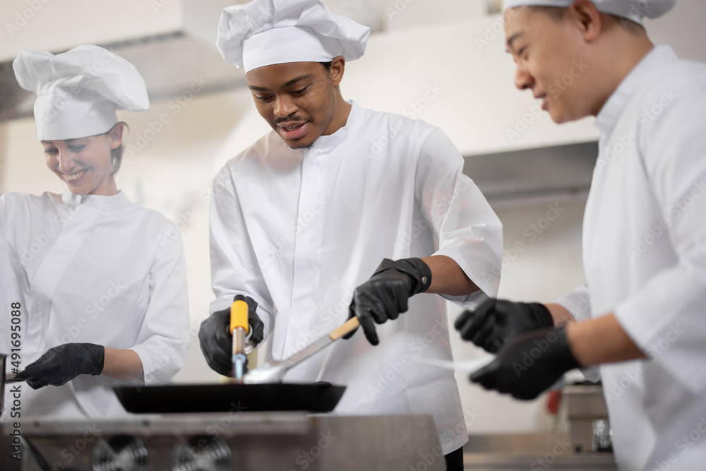 身着制服的多种族专业厨师团队在厨房为餐厅做饭。a