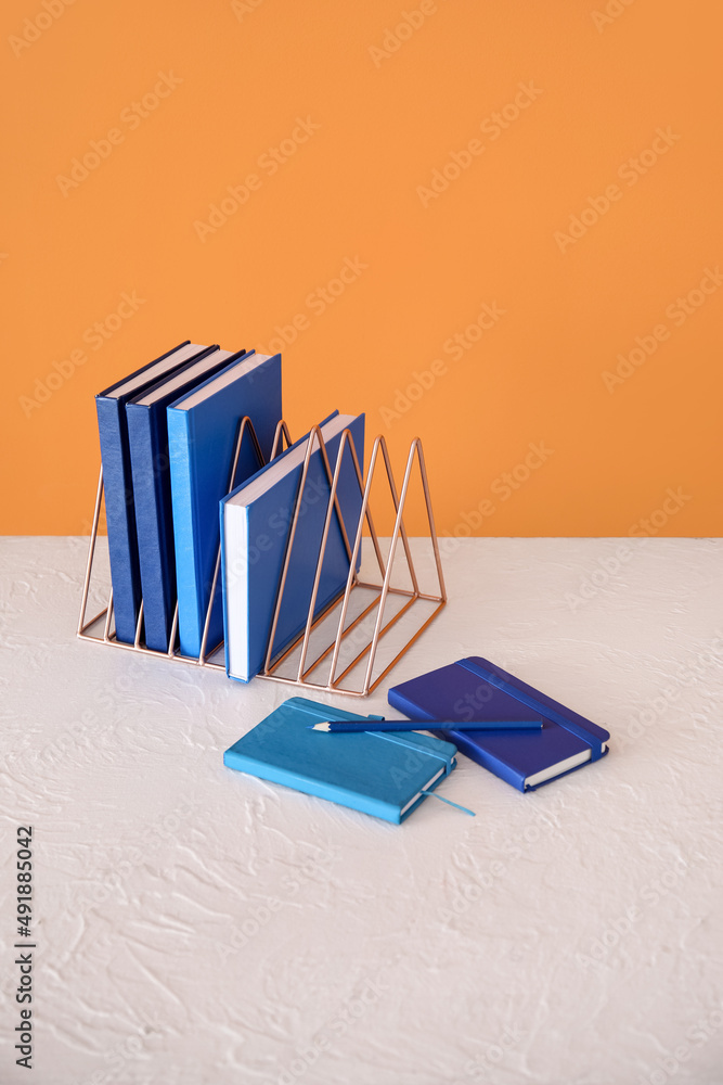 Metal organizer with books on table against orange background