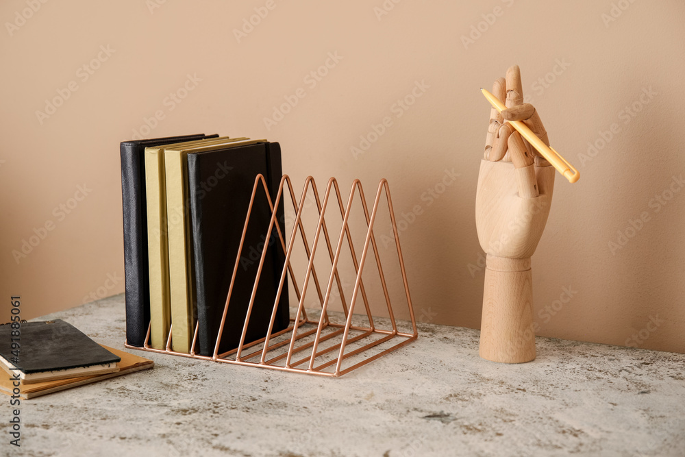 Metal organizer with books and wooden hand on table against beige background