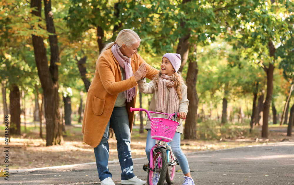 骑自行车的小女孩在秋季公园向奶奶击掌