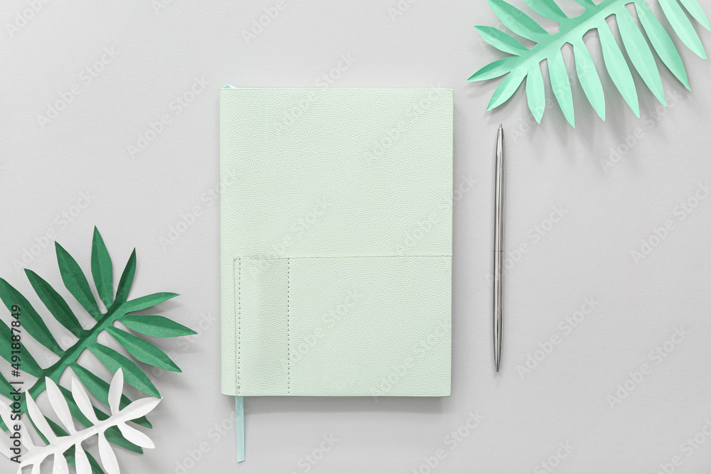 时尚笔记本，浅色背景上有笔和纸棕榈叶
