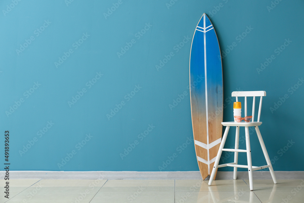 一瓶防晒霜、椅子上的太阳镜和房间彩色墙附近的冲浪板