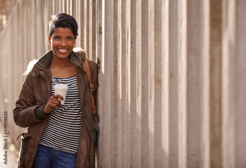Got my coffee, ready to go. A portrait of a beautiful young woman leaning against a concrete wall in