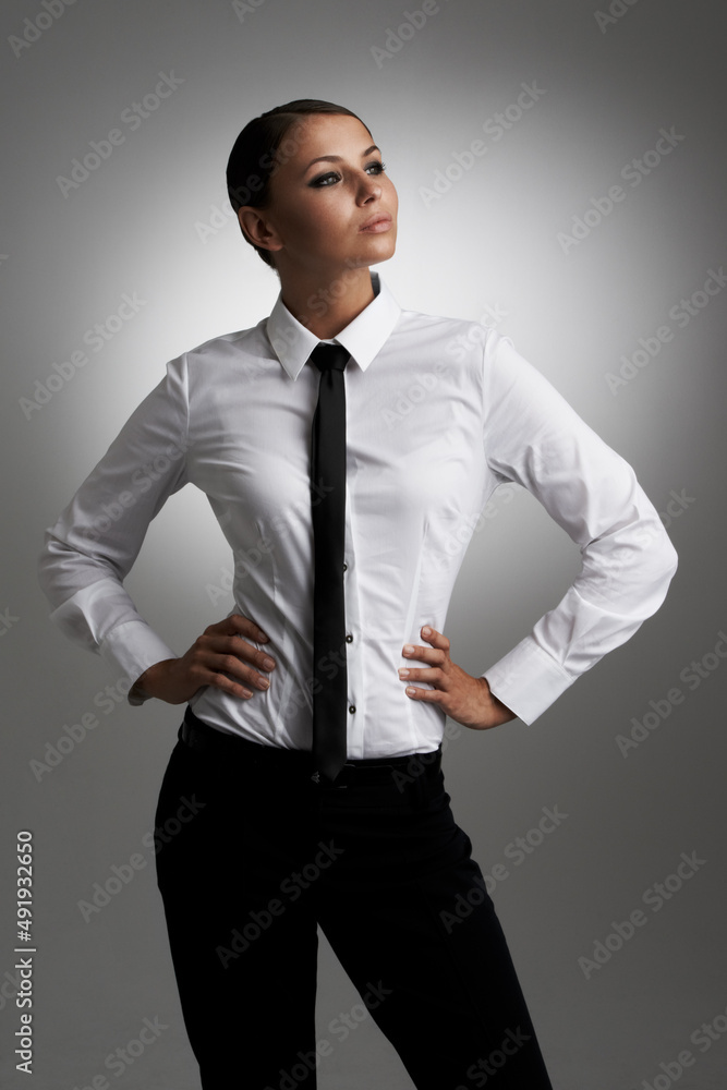 对自己的风格充满信心。一位身穿衬衫、打着领带的年轻女子双手放在h上，侧身看着。
