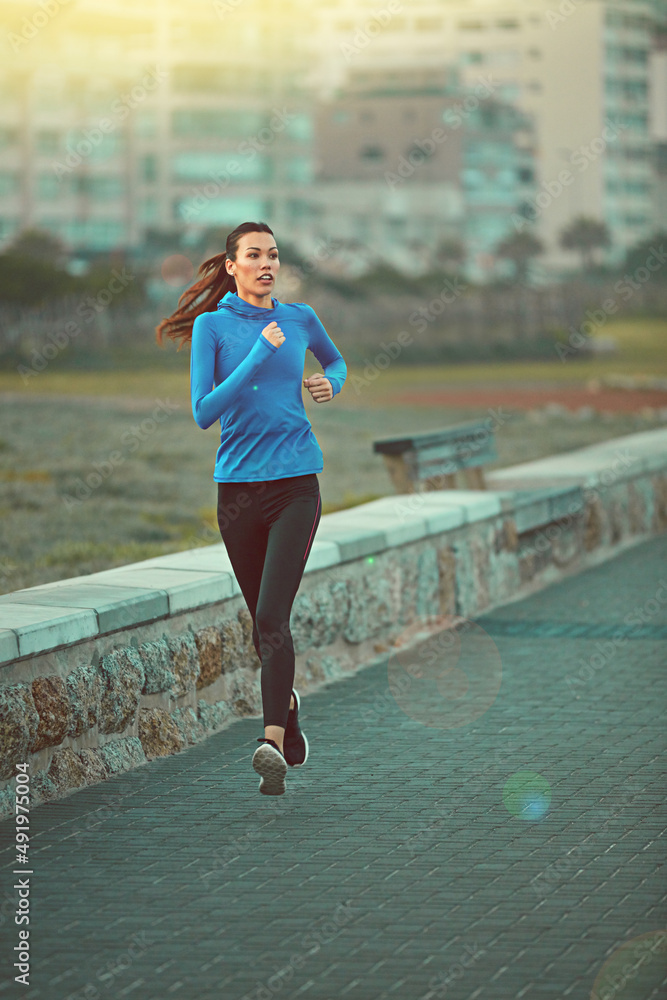 跑步是一种放松。一个运动型年轻女子在海滨大道上跑步的照片。