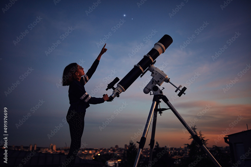 带着天文望远镜的女孩在黄昏的天空下观星。