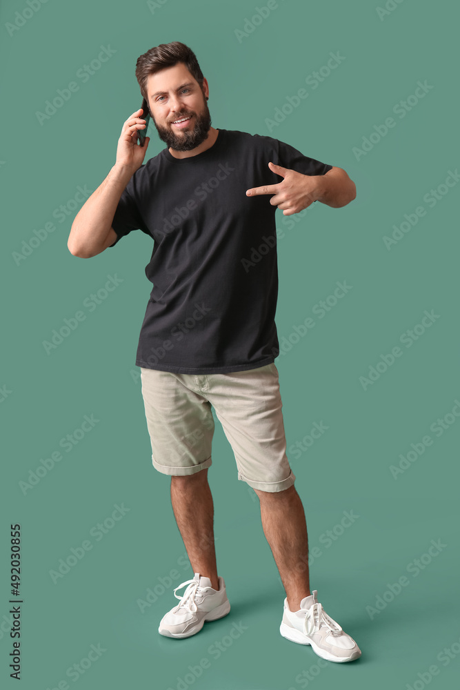 身穿黑色t恤的英俊男子在绿色背景下用手机通话