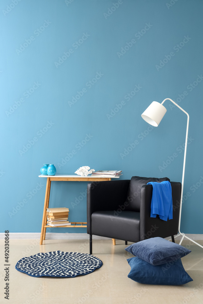 现代扶手椅、落地灯、带书的桌子和彩色墙附近的装饰