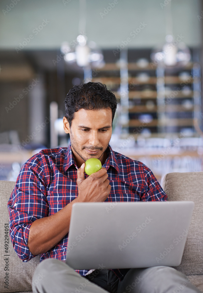保持零食健康。一个年轻人在家里用笔记本电脑工作时正在吃苹果。