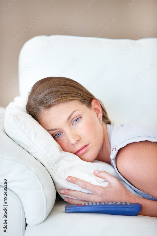太无聊了……漂亮的年轻女人躺在沙发上，手里拿着电视遥控器，看起来很难过。