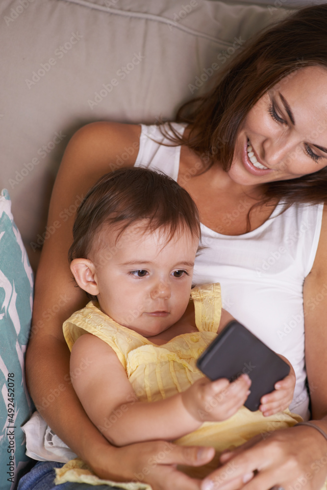 她太好奇了。一个女婴躺在妈妈的腿上玩手机。