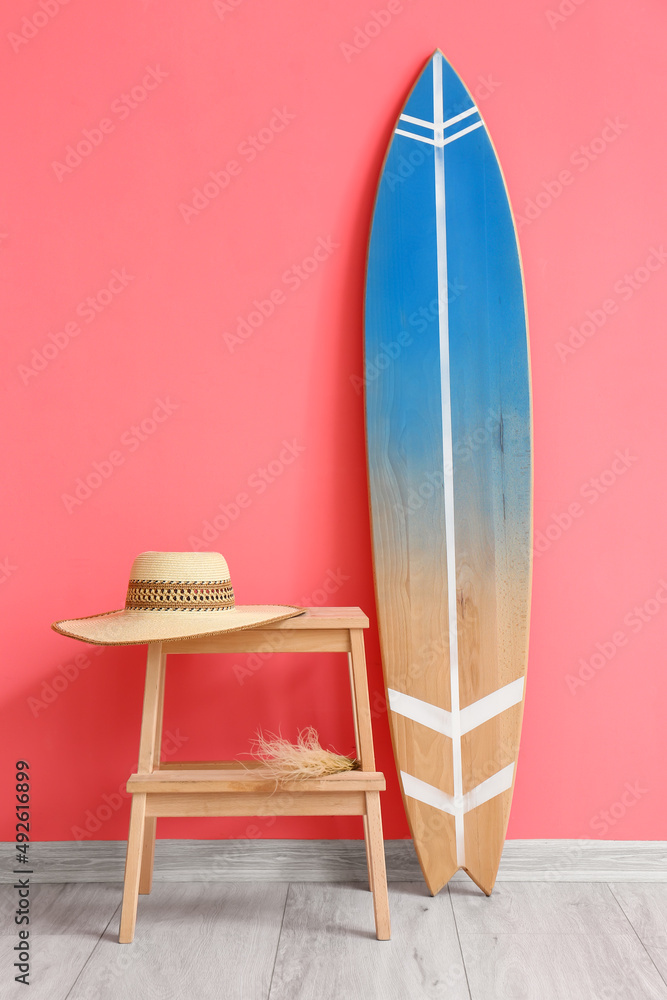 粉红色墙壁附近的木制冲浪板和带帽子的桌子