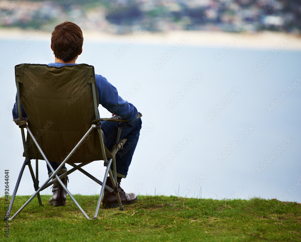 欣赏风景的最佳地点。一个年轻人坐在露营椅上观看的后视图
