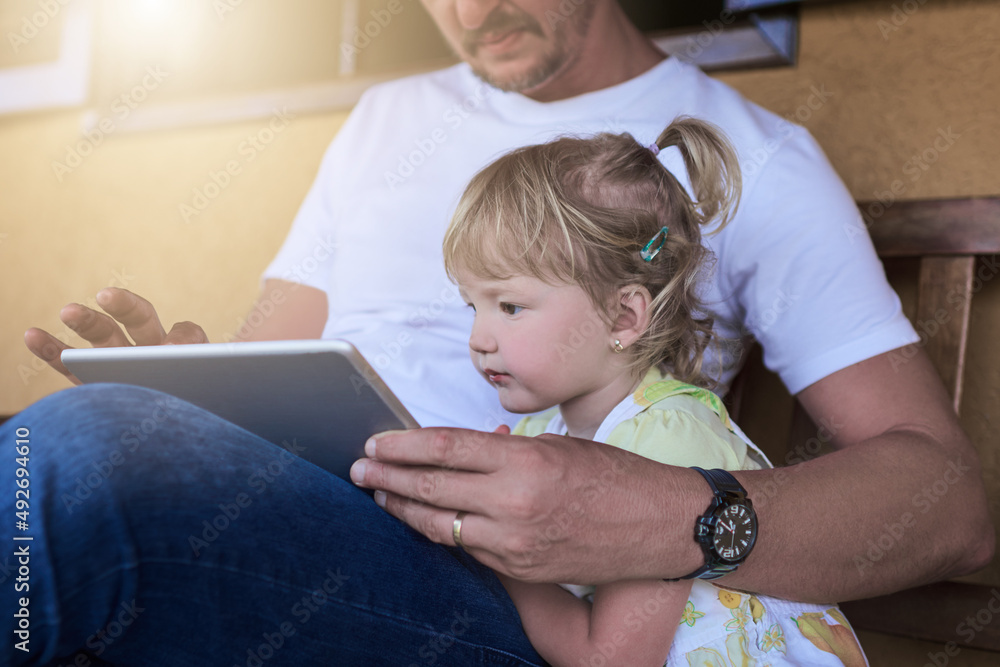 她很想了解更多。一位父亲和他的小女儿一起使用数字平板电脑的照片