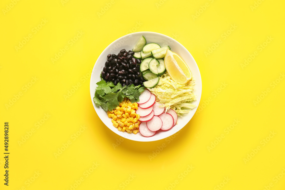 Bowl with ingredients for Mexican vegetable salad on yellow background